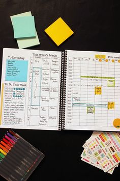 an open planner with sticky notes, markers and crayon stickers next to it