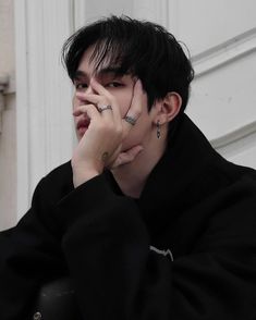 a young man with black hair and piercings on his face sitting in front of a white door