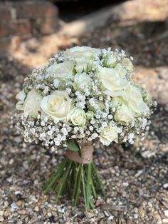 a bouquet of white roses and baby's breath sits on the ground next to gravel