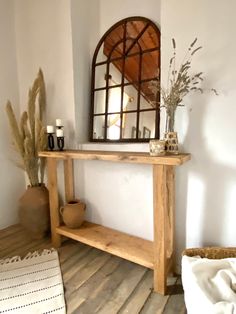 a wooden table sitting on top of a hard wood floor next to a vase and mirror