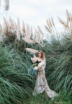 a woman standing in tall grass holding a bouquet