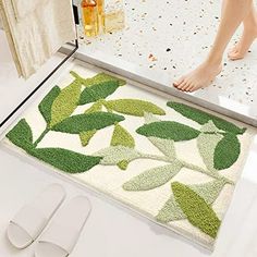 a bathroom rug with leaves on it next to a pair of slippers and a shower door mat