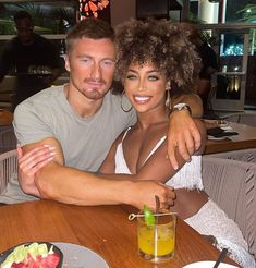 a man and woman sitting at a table with drinks in front of them, posing for the camera