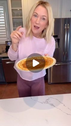 a woman is holding a plate with pancakes on it and pointing to the camera while standing in front of a refrigerator