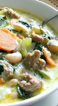 a white bowl filled with soup and meat on top of a table next to a spoon