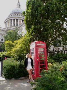 a woman standing next to a red phone booth