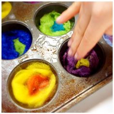 a child's hand picking up colored play dough from a muffin tin tray