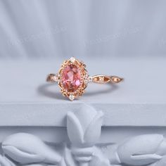 an oval shaped pink sapphire and diamond ring on top of a white marble pedestal with flowers