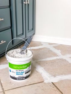 a bucket of white paint sitting on the floor next to a blue cabinet and drawers