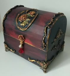 an ornate wooden box with gold trimmings and red flowers on the lid is sitting on a white surface