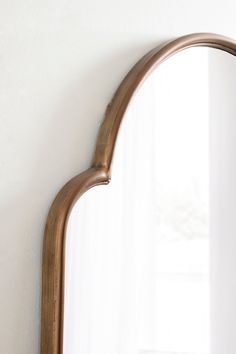 an arched mirror hanging on the wall in front of a white wall with a window behind it