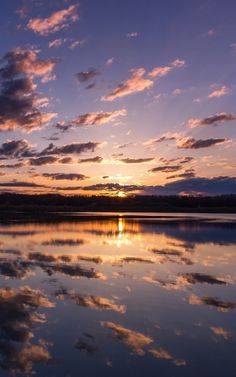 the sun is setting over water with clouds in the sky and reflecting it's reflection