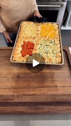 a woman standing in front of a wooden cutting board holding a pan filled with food