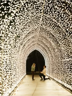 two people are sitting in the middle of a tunnel covered with lights