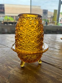 a yellow glass candle holder sitting on top of a wooden table