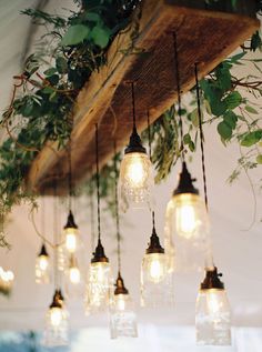 mason jar chandelier with hanging lights and greenery on the ceiling above it