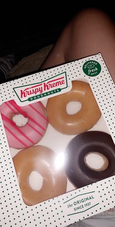 three doughnuts in a krispy kreme box sitting on someone's lap