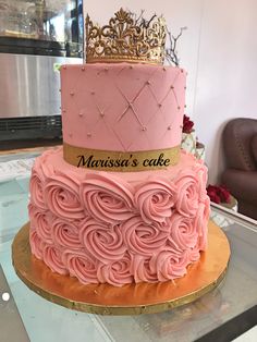 a three tiered cake with pink frosting and gold trimmings, topped with a crown