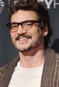 a close up of a person wearing glasses and a cardigan sweater with a smile on his face