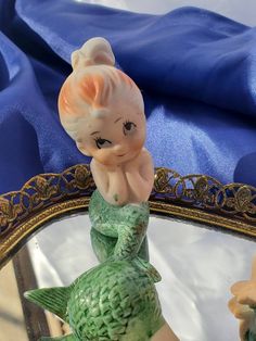 a little figurine sitting on top of a mirror next to a blue cloth