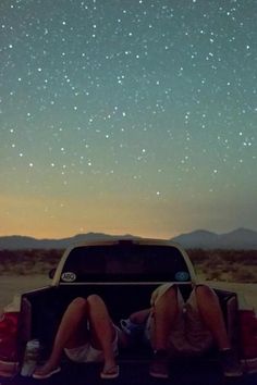 two people sitting in the back of a pick up truck under a night sky filled with stars