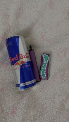 a can of red bull energy drink next to a battery on a white bed sheet