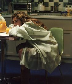 a woman sitting at a table covered in a blanket next to a bottle of orange juice