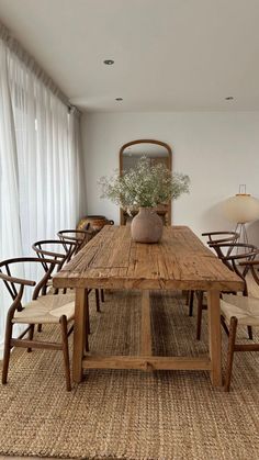 a dining room table with chairs and a vase on top of it in front of a window