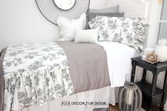 a bedroom with white and gray bedding, black side table and mirror on the wall