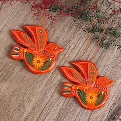 two orange bird ornaments hanging from strings on a wooden table with red flowers and greenery