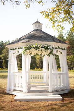 a gazebo with white curtains and flowers on it