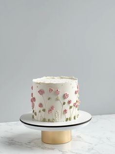 a white cake with pink flowers on it sitting on a gold plate and grey background