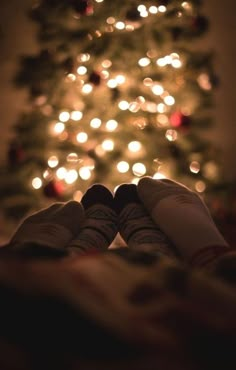 someone is holding their feet up in front of a christmas tree with lights on it