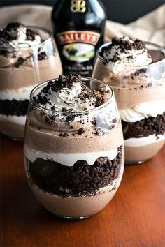 three glasses filled with dessert sitting on top of a wooden table next to a bottle