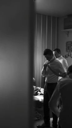 two men are standing in a room and one is adjusting his tie while the other man looks on