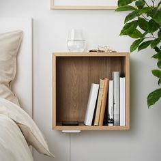 a wooden shelf with books on it next to a bed and a potted plant