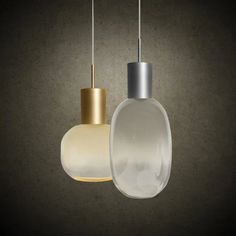 two white and gold pendant lights hanging from the ceiling in a dark room with concrete walls