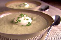 two bowls of soup with sour cream and chives on the top one has spoons