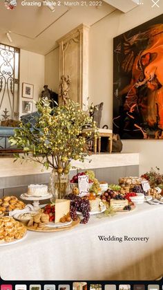 a table covered with food and flowers in front of a large painting on the wall