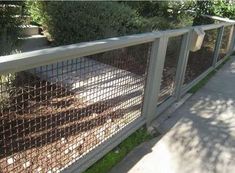 a fence that has some plants growing on top of it in front of a sidewalk