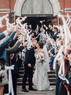 a bride and groom are walking down the stairs with their guests holding streamers in front of them