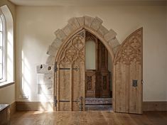 an arched wooden door in the middle of a room with wood floors and windows on both sides