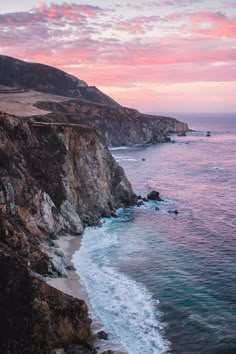 an ocean cliff with waves crashing on the shore and pink clouds in the sky above