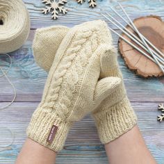 a woman's hands in mitts next to some yarn and snowflakes