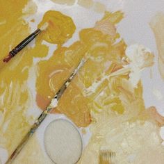 two paintbrushes sitting on top of a table next to some yellow and white paints