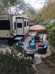 an rv is parked in the backyard with chairs, tables and umbrellas around it