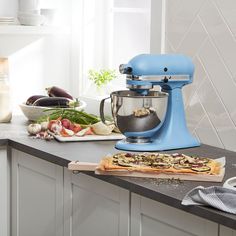 an image of a kitchen scene with focus on the mixer and ingredients in the background