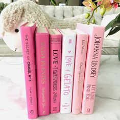 three pink books sitting on top of a white table next to a stuffed animal and flowers