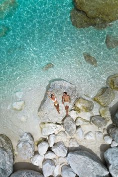 two people are laying on rocks in the water