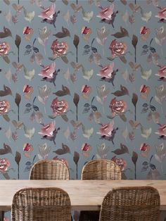 a dining room table with wicker chairs and a wallpapered floral pattern behind it